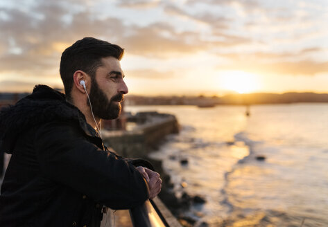 Spanien, Gijon, bärtiger Mann hört Musik mit Kopfhörern bei Sonnenuntergang - MGOF001622