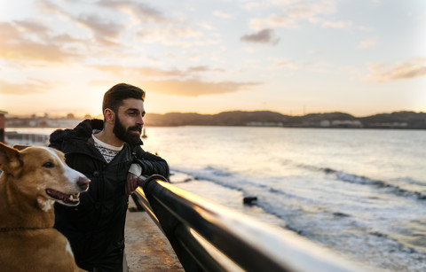 Lächelnder Mann und sein Hund bei Sonnenuntergang, lizenzfreies Stockfoto