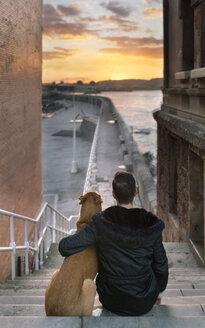 Spanien, Gijon, Rückenansicht eines Mannes und seines Hundes, die auf einer Treppe sitzen und den Sonnenuntergang beobachten - MGOF001624