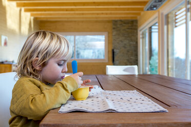 Little boy sitting at wooden table eating something - ZOCF000009