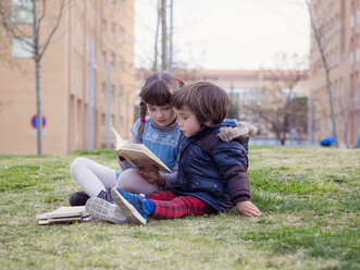 Little girl sitting with her brother on a meadow watching a book - XCF000067