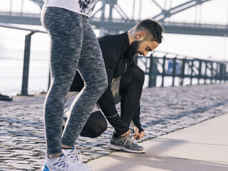 Germany, Cologne, Young couple, workout, man tying shoes - MADF000866