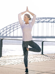 Germany, Cologne, young woman practicing yoga, tree position - MADF000874