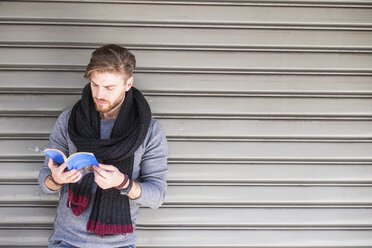 Mann mit Schal steht vor einem Rollladen und liest ein Buch - SIPF000264