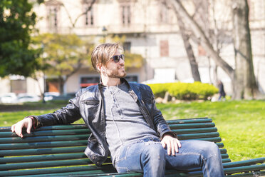 Mann mit Sonnenbrille und Kopfhörern entspannt auf einer Parkbank - SIPF000265