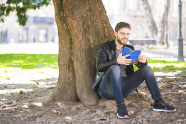 Mann sitzt vor einem Baumstamm und liest ein Buch - SIPF000267