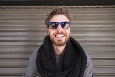 Porträt eines grinsenden Mannes mit blauer Sonnenbrille vor einem Rolltor - SIPF000270