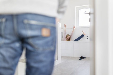 Frau sitzt in der Badewanne ihres neuen Hauses und weint vor Freude, während ihre Freundin sie beobachtet, lizenzfreies Stockfoto