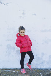 Portrait of smiling little girl with hands in pockets in front of a wall - ERLF000149