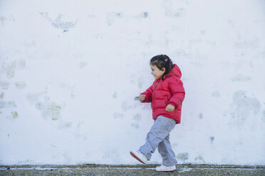Lächelndes kleines Mädchen spielt vor einer Mauer - ERLF000150