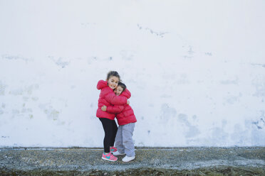 Two happy little sisters hugging each other in front of a wall - ERLF000154