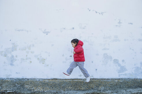 Kleines Mädchen läuft vor einer Mauer - ERLF000156