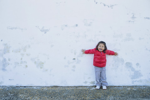Porträt eines kleinen Mädchens, das sich mit ausgestreckten Armen anlehnt und die Zunge herausstreckt, lizenzfreies Stockfoto