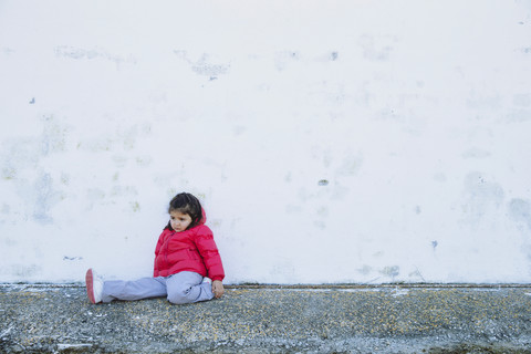 Sad little girl sitting in front of a wall stock photo