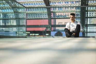 Portrait of waiting young businessman sitting on the ground - SIPF000288