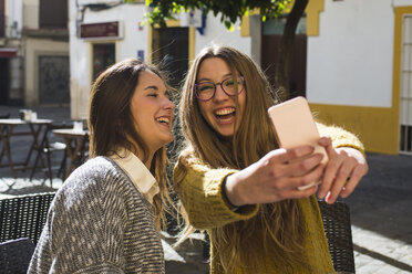 Lachende junge Frau, die ein Selfie mit ihrer Freundin in einem Straßencafé macht - KIJF000250