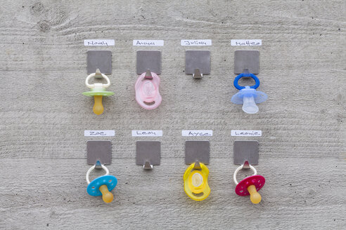 Pacifiers hanging on concrete wall with name tags - WDF003578