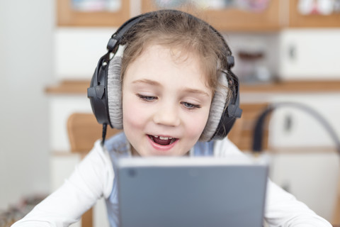 Porträt eines kleinen Mädchens mit Kopfhörern, das etwas auf einem digitalen Tablet sieht, lizenzfreies Stockfoto
