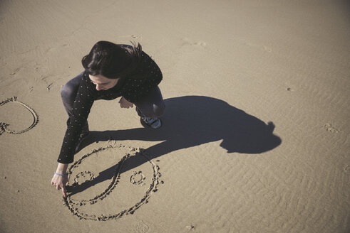 Frau kratzt Yin-Yang-Symbol in den Sand eines Strandes - EPF000040