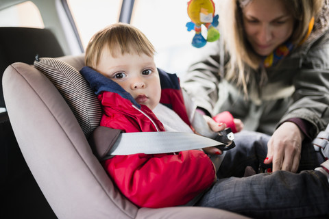 Frau befestigt Sitzglocke seines kleinen Sohnes im Kindersitz im Auto, lizenzfreies Stockfoto