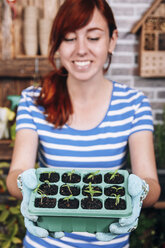 Young woman holding container with tomato seedlings - RTBF000047
