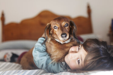 Smiling little boy lying on bed with long-haired Dachshund - VABF000380