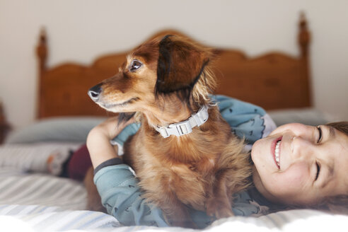 Smiling little boy lying on bed with long-haired Dachshund - VABF000381