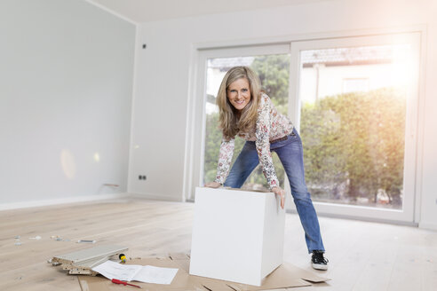 Porträt einer lächelnden Frau, die einen Schrank in einem Zimmer ihrer neuen Wohnung zusammenbaut - SHKF000584