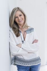 Portrait of smiling blond woman with arms crossed leaning against wall - SHKF000587