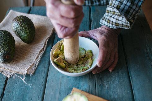 Hände eines Mannes, der Avocado für Guacamole zerdrückt - KIJF000269