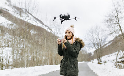 Spanien, Asturien, junge Frau, die eine Drohne in den verschneiten Bergen steuert - MGOF001631