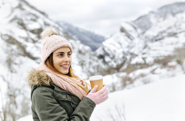 Spanien, Asturien, glückliche junge Frau mit Kaffee zum Mitnehmen in den verschneiten Bergen - MGOF001638