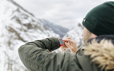 Spanien, Asturien, junger Mann mit Smartwatch in den verschneiten Bergen - MGOF001640