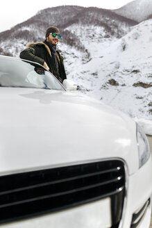 Spanien, Asturien, Mann lehnt an seinem Auto in den verschneiten Bergen - MGOF001644
