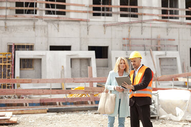 Mann mit Schutzhelm im Gespräch mit Frau auf einer Baustelle - MAEF011385