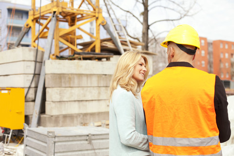 Frau sieht Mann mit Schutzhelm auf Baustelle an, lizenzfreies Stockfoto