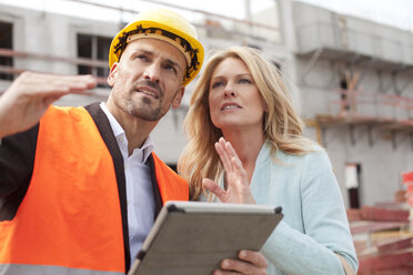 Man with hard hat talking to woman on construction site - MAEF011388