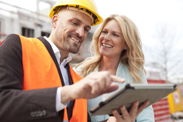 Smiling man with hard hat talking to woman on construction site - MAEF011389