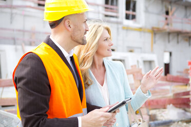 Man with hard hat talking to woman on construction site - MAEF011394
