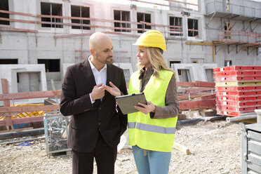 Woman with hard hat talking to man on construction site - MAEF011396