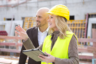 Woman with hard hat talking to man on construction site - MAEF011397