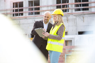 Woman with hard hat and digital tablet and man on construction site - MAEF011398