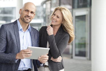 Geschäftsmann und lächelnde Geschäftsfrau mit digitalem Tablet im Freien - MAEF011402