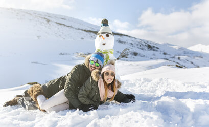 Spanien, Asturien, glückliches Paar im Schnee liegend neben einem Schneemann - MGOF001673