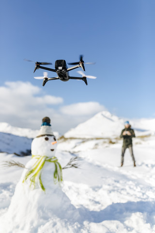 Spanien, Asturien, Mann fliegt Drohne in verschneiten Bergen, lizenzfreies Stockfoto