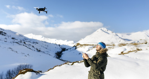 Spanien, Asturien, Mann fliegt Drohne in verschneiten Bergen, lizenzfreies Stockfoto