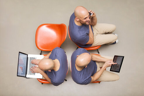 Man sitting on chairs using portable devices, multitasking - MAEF011426