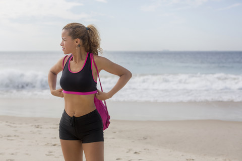 Sportliche Frau steht am Strand und schaut in die Ferne, lizenzfreies Stockfoto