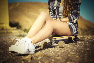 Teenage girl sitting on longboard, partial view - SIPF000294