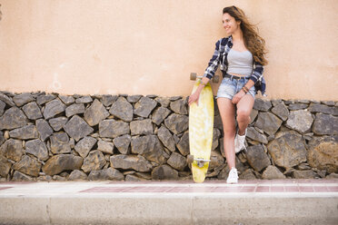 Portrait of smiling teenage girl with longboard leaning against wall - SIPF000309
